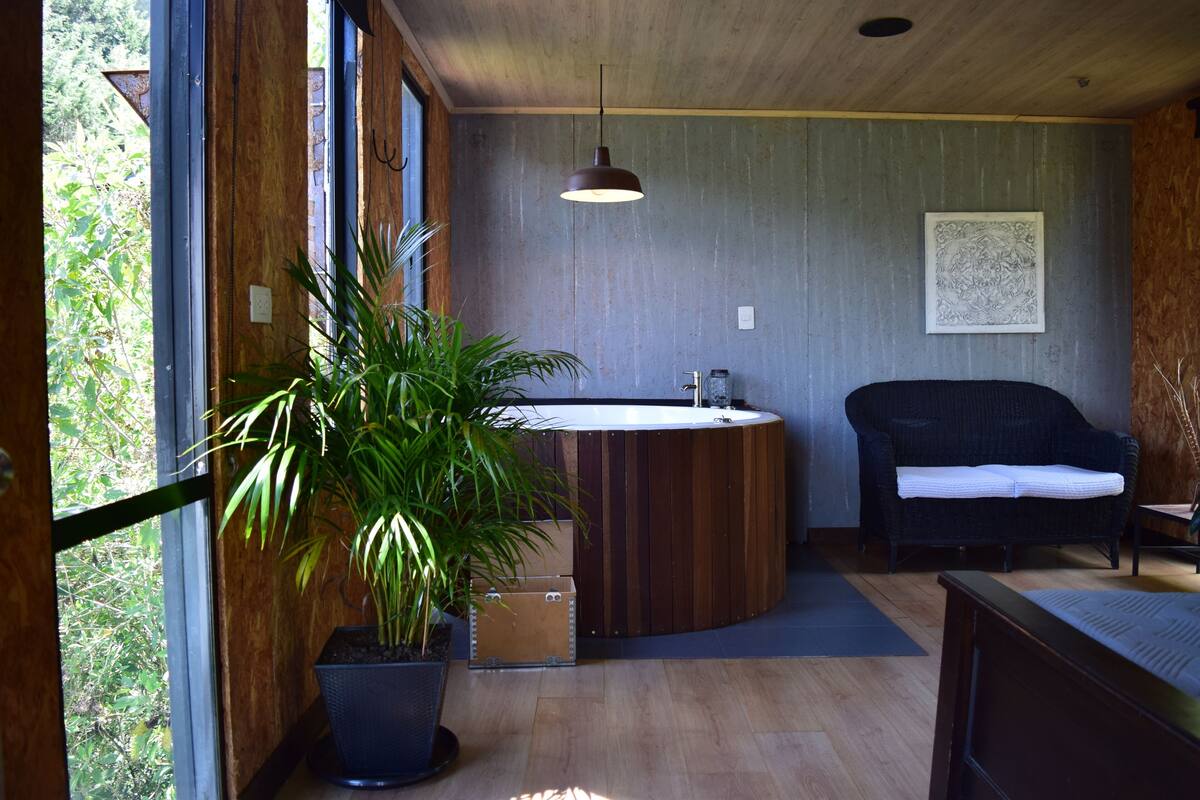 Ein modernes Badezimmer mit einem Holz-Waschtisch, einer großen Kübelpflanze und einem schwarzen Stuhl.
