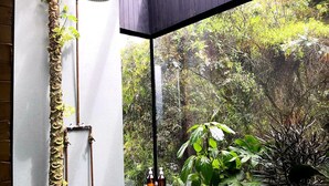 Ein Badezimmer mit Dusche, Fenster und Blick auf einen Wald.