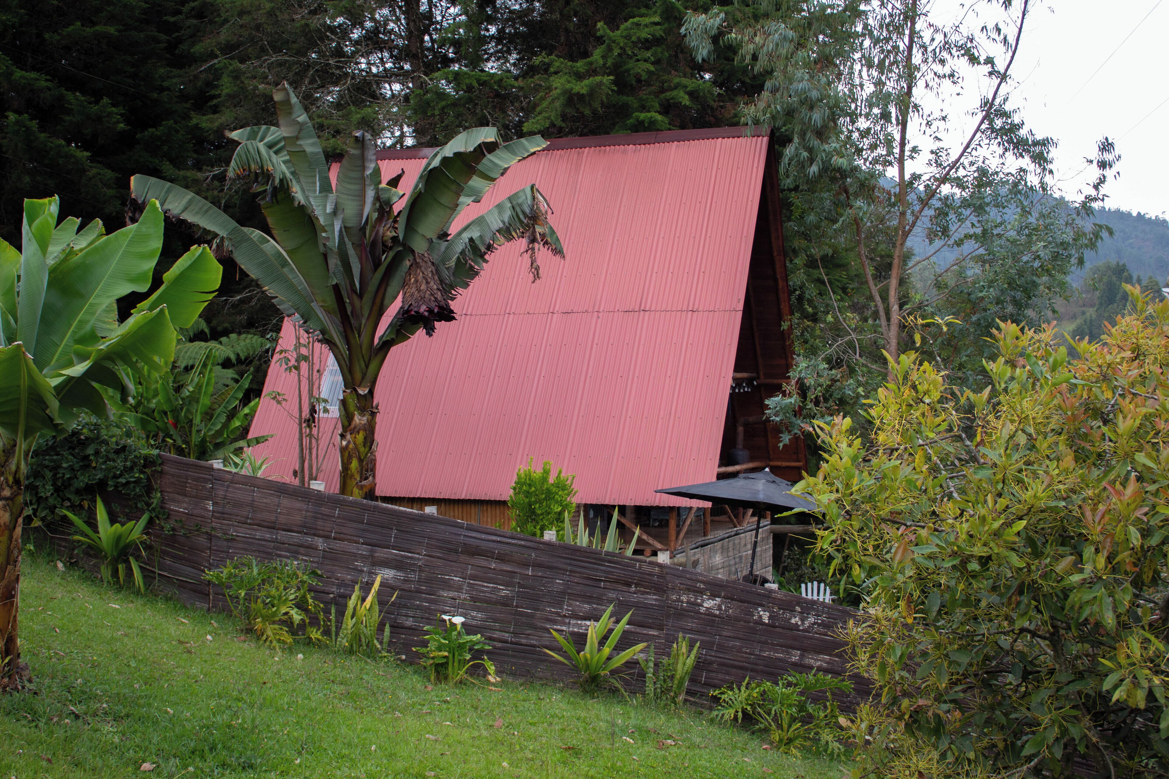 A red building with a sloped roof, surrounded by lush greenery and a wooden fence.