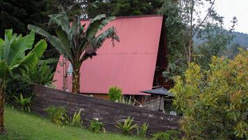 A red building with a sloped roof, surrounded by lush greenery and a wooden fence.