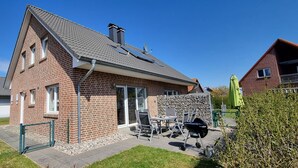 Una casa de ladrillo de dos pisos con techo inclinado, paneles solares y un patio con mobiliario exterior.