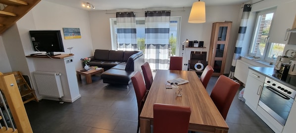 A modern kitchen with a dining area, a sofa, and a TV.