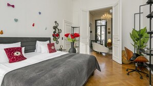 Un dormitorio con una cama grande, un escritorio y una silla. Hay una puerta que da a otra habitación.