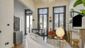 Una sala de estar moderna con un sofá blanco, una zona de comedor con mesa y sillas, y una chimenea con una lámpara decorativa.