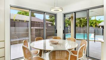 A modern dining area with a round table and wicker chairs, large sliding glass doors leading to a pool.
