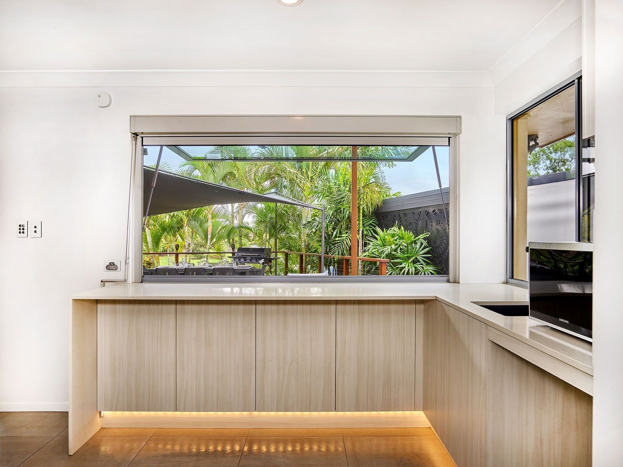 A modern kitchen with a large window overlooking a tropical garden.