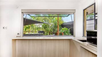 A modern kitchen with a large window overlooking a tropical garden.