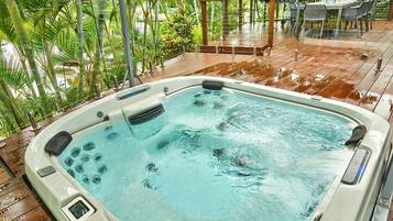 A hot tub surrounded by lush greenery and a dining area with tables and chairs.