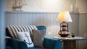 Een teal fauteuil met gestreepte kussens, een scheepsmodel aan de muur en een tafel met een lamp en een kleine plant.