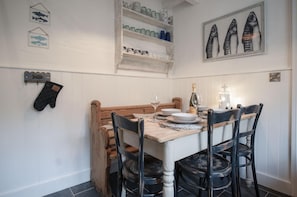 A dining area with a wooden table set for four, surrounded by black chairs with intricate designs. Above the table, there are shelves with glassware and a framed fish illustration.
