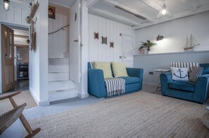 A living room with a blue sofa, a wooden chair, a staircase, and a kitchen area with an oven.