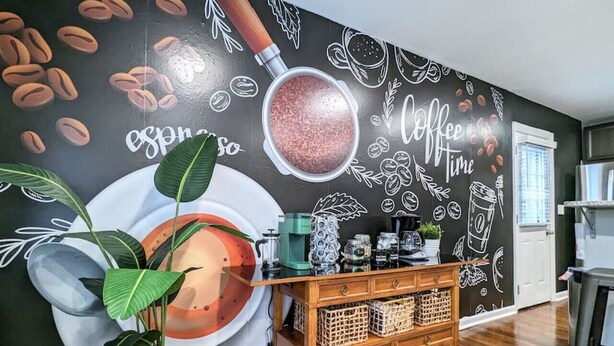 Een kamer met een muurschildering over koffie, een houten kast en een potplant.