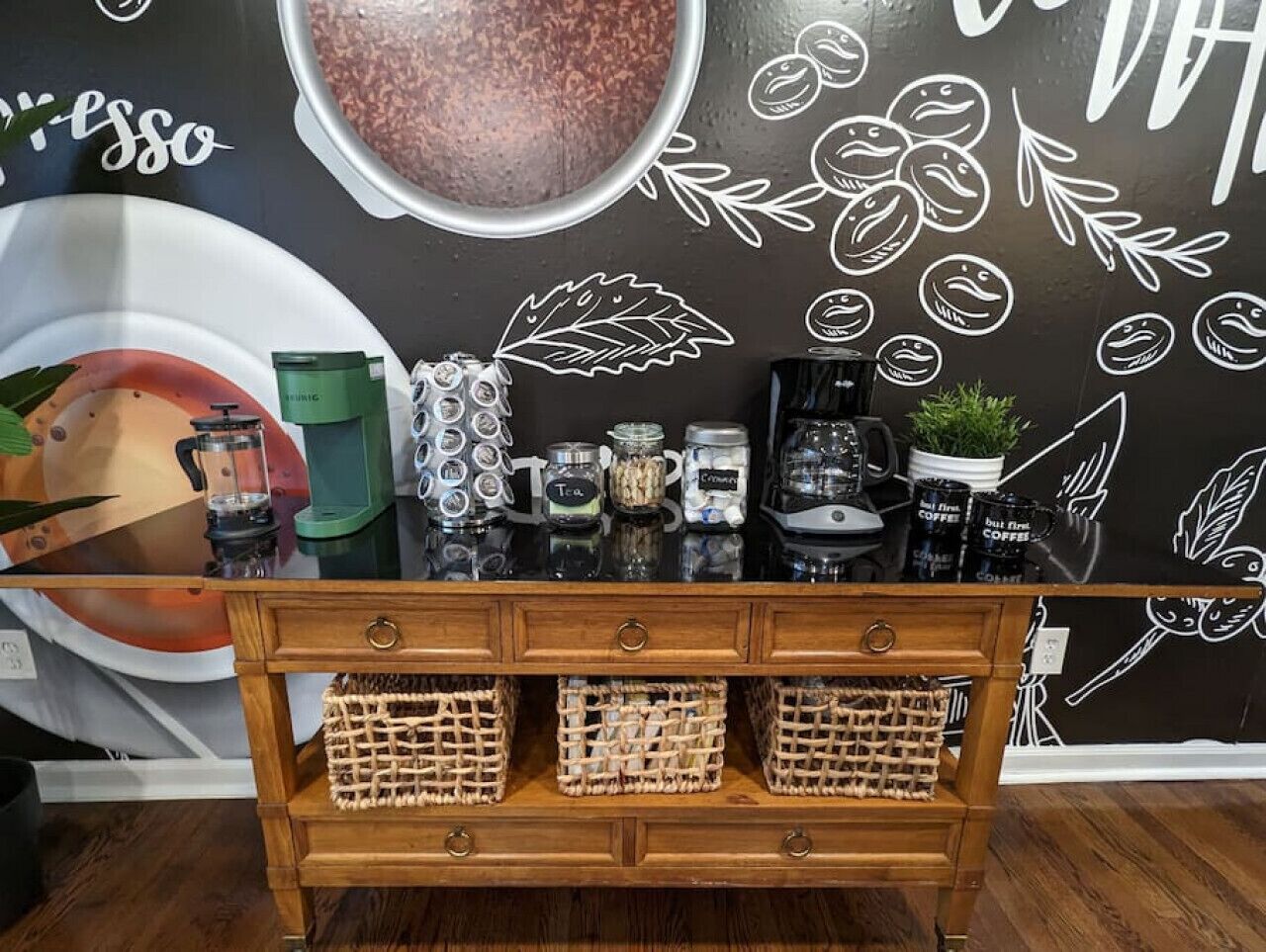 Mostrador de cafetería con diseño rústico de madera, que incluye una máquina de café, tarros y una pared decorativa con ilustraciones sobre café.