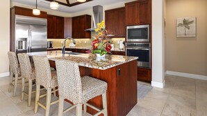 A modern kitchen with wooden cabinets, stainless steel appliances, and a central island with bar stools. - Holua Kai#8  w/ Private Pool, Ocean & Golf Views, Community Pool & Spa (Kailua-Kona)