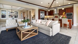 A spacious living room with a sofa, coffee table, and a dining area with a kitchen in the background. - Holua Kai#8  w/ Private Pool, Ocean & Golf Views, Community Pool & Spa (Kailua-Kona)