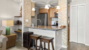 Una cocina con una isla central, taburetes de bar, un refrigerador y un microondas.