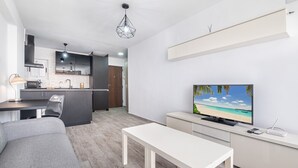 A modern living space with a kitchen, dining area, and a TV displaying a beach scene. - Karola Apartment 12-C Levante Beach (Benidorm)