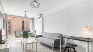 A modern living room with a sofa, a dining table, and chairs. There is a large window with a view of the city. - Karola Apartment 12-C Levante Beach (Benidorm)