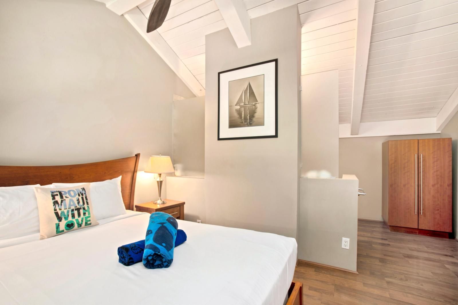 Ein Hotelzimmer mit einem großen Bett, einem Nachttisch mit Lampe, einem gerahmten Bild an der Wand und einem Holzschrank.