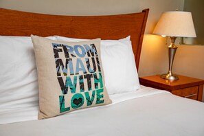 Un lit avec un oreiller orné de l’inscription « AVEC AMOUR, DE MAUI » et une lampe de chevet.