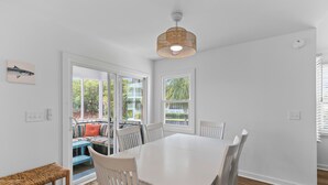 A dining area with a white table and chairs, a woven ceiling light, and a view of a patio with a bench and railing. - Pelican Bay 13 - Brand New Reno! 1 Block to Beach! (Isle of Palms)