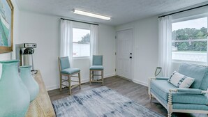 A room with a coffee machine, two chairs, a sofa, and a view of a dock and trees. - Dockside Inn (Deltaville)