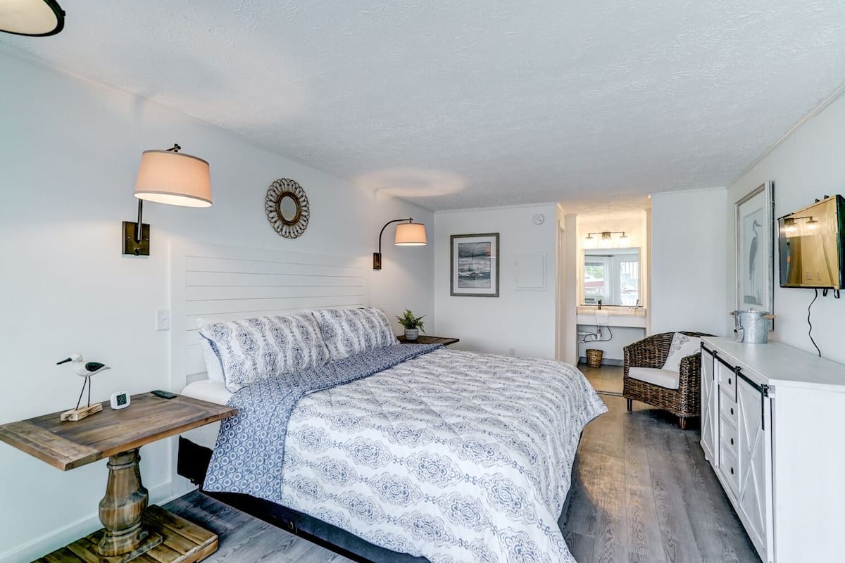 A bedroom with a bed, bedside table, lamp, and a view of the bathroom.