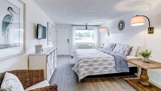 A bedroom with a bed, a bedside table, a lamp, a TV, and a window. - Dockside Inn (Deltaville)
