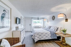 A bedroom with a bed, a bedside table, a lamp, a TV, and a window.