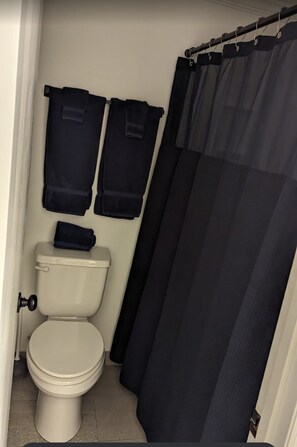 A small bathroom with a toilet, a shower curtain, and two towels hanging on the wall.