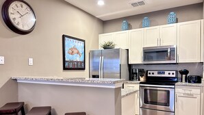 Una cocina con armarios blancos, electrodomésticos de acero inoxidable, encimera de granito y un reloj en la pared.