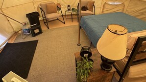 Una carpa con una cama, una silla, una mesita, una lámpara y un calentador portátil.
