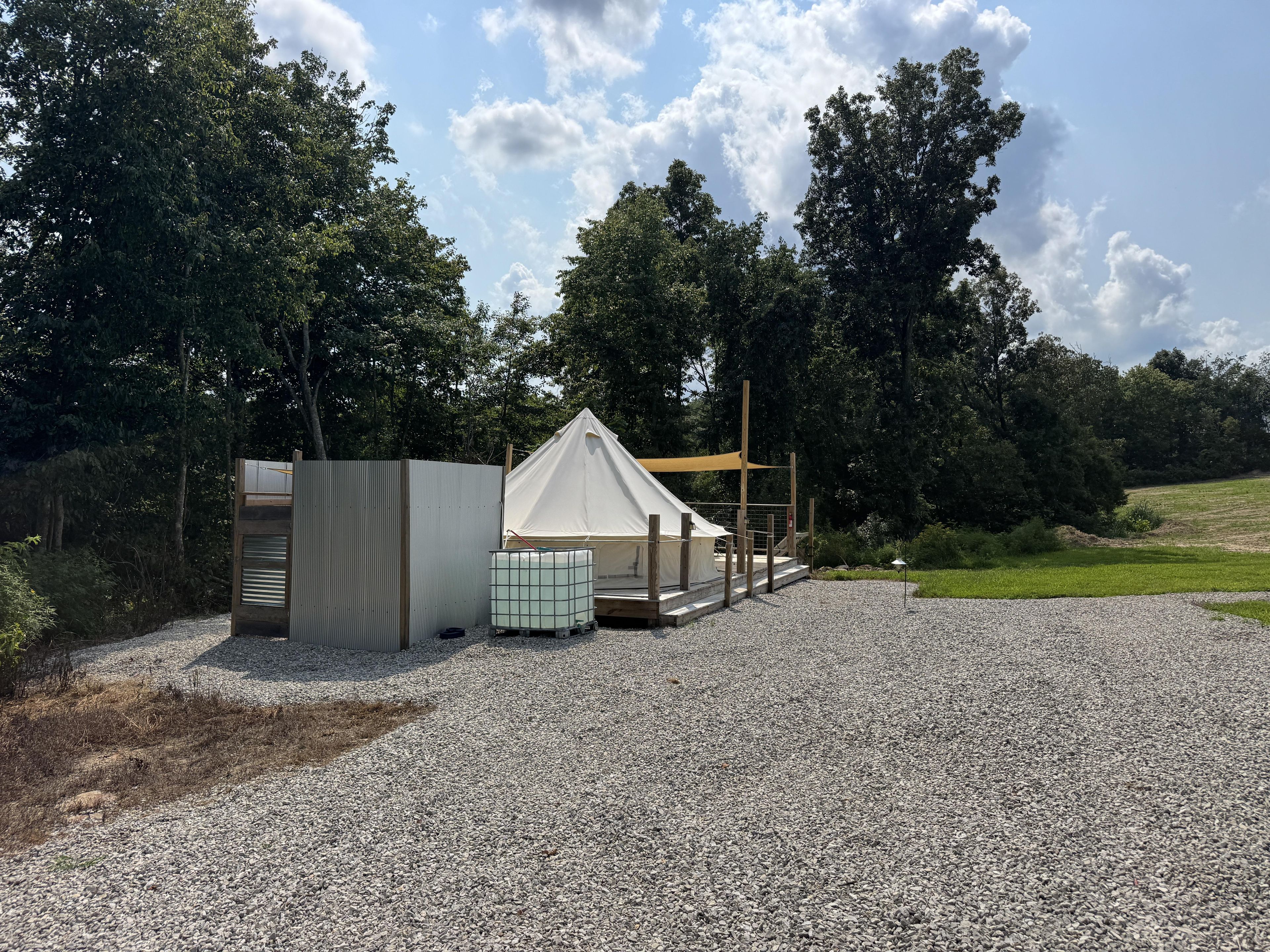 Alojamiento en carpa sobre suelo de grava, rodeado de árboles y una zona ajardinada.