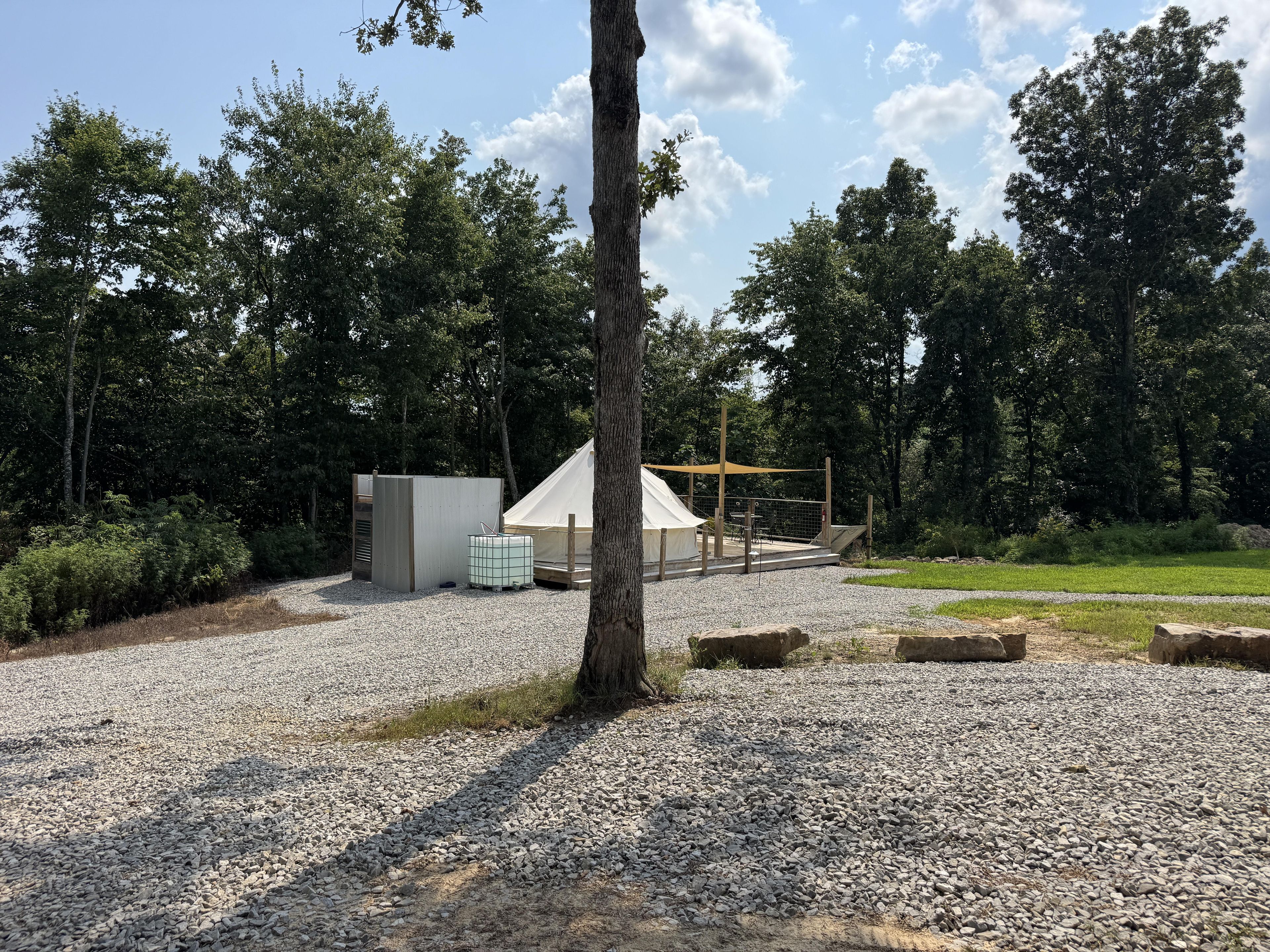 A campsite with a tent, a small utility shed, and a gravel path.