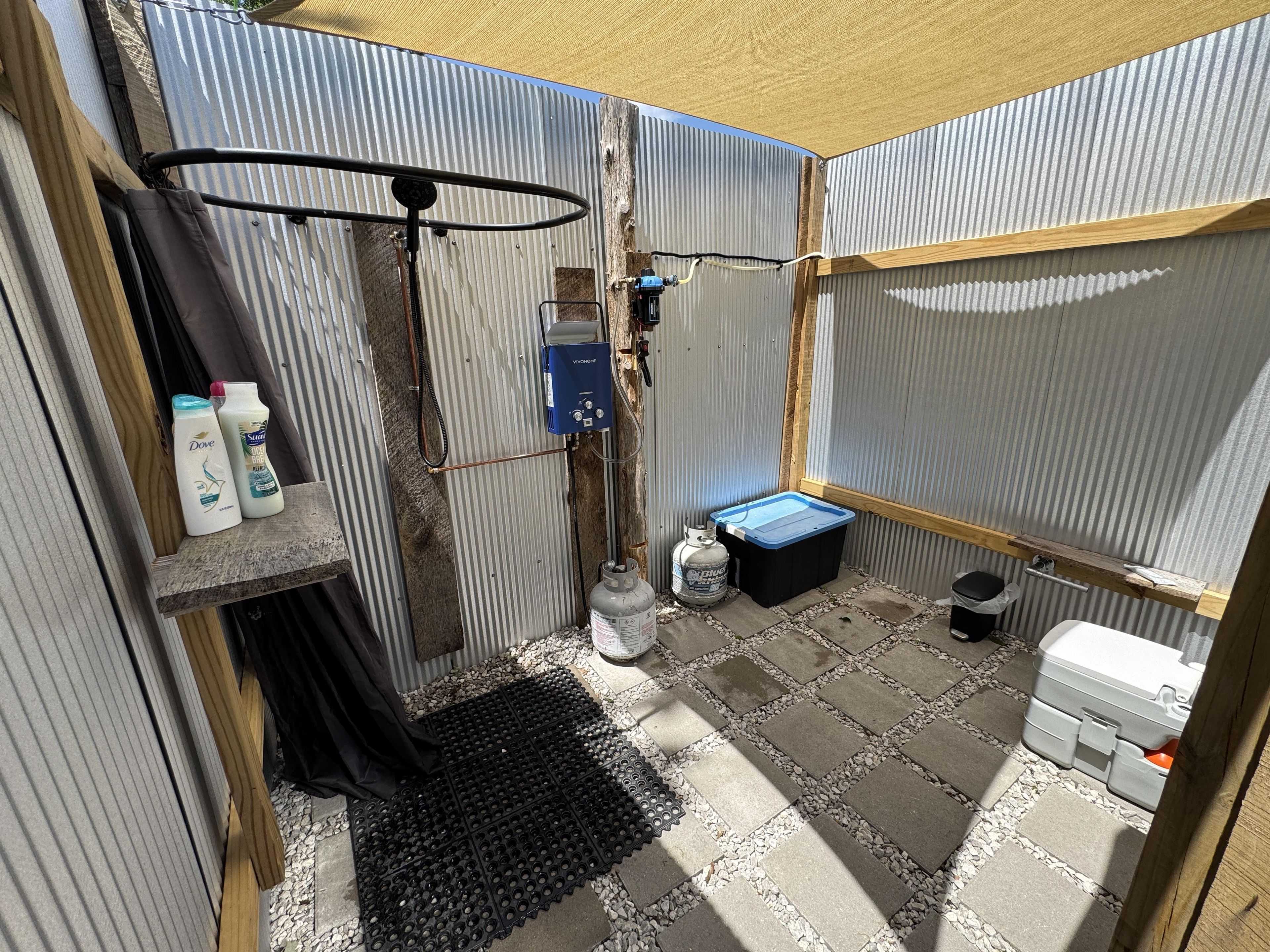 Un baño pequeño con ducha, calentador de agua y un contenedor de almacenamiento.