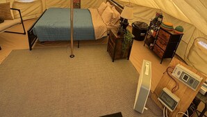Una carpa con una cama, una lámpara, un aparador y una pequeña mesa con dispositivos electrónicos.