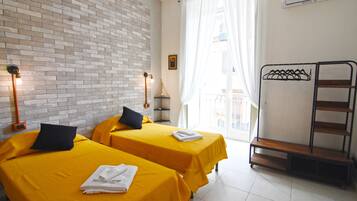 A hotel room with two beds, a brick wall, a window with curtains, a metal shelf, and a wall-mounted air conditioner.