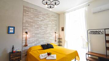 Una habitación de hotel con cama, mesita de noche, lámpara de pared, perchero y ventana con cortinas.
