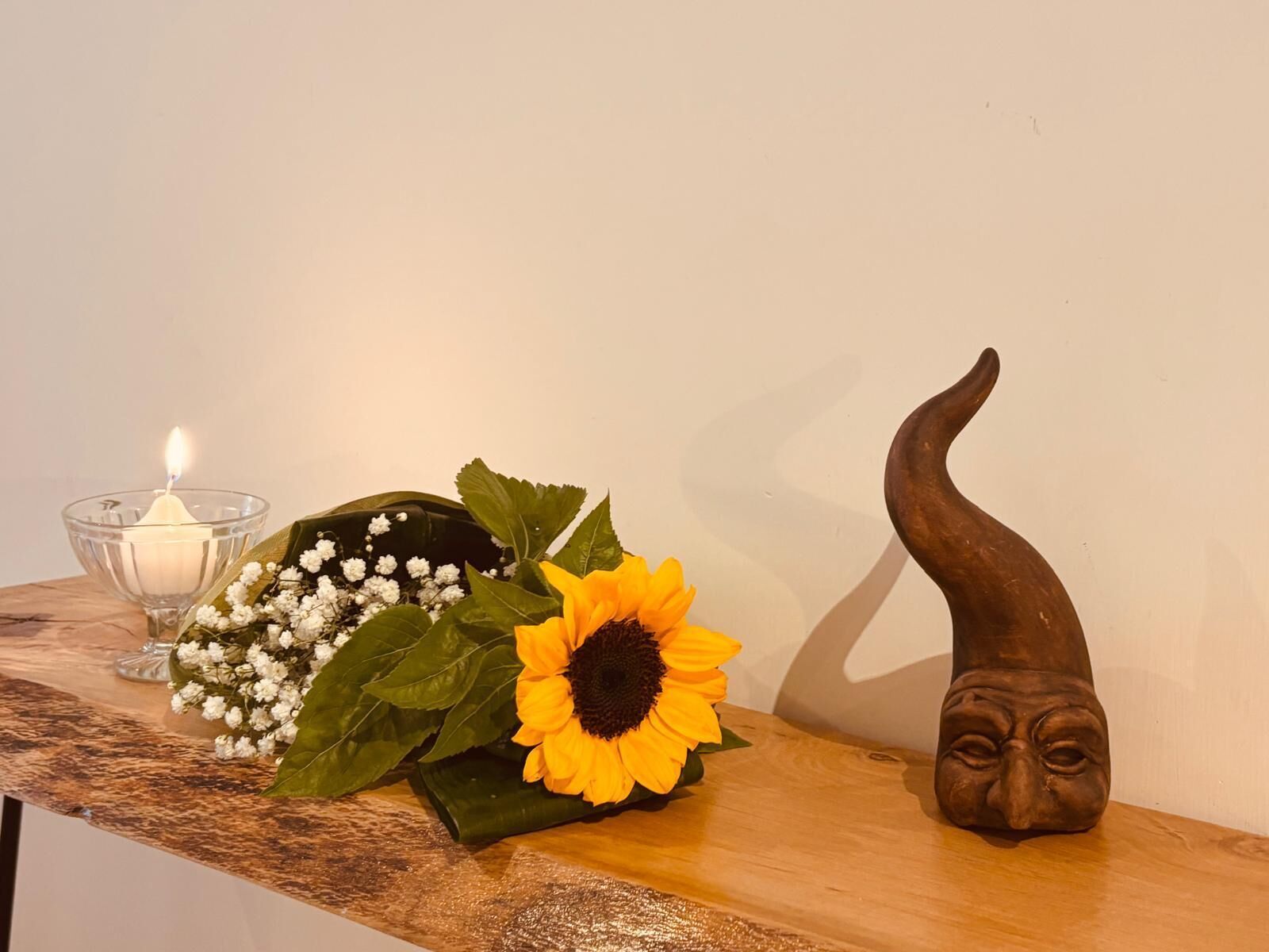 A wooden table with a lit candle, a bouquet of flowers, and a carved wooden figure.