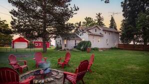 Un jardin avec un foyer et des fauteuils Adirondack rouges, un garage rouge et une maison avec une cheminée.