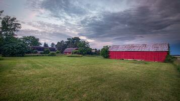 A rural landscape with a red barn, a smaller red building, and a grassy field under a cloudy sky.