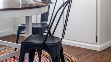 Ett kök med ett runt bord, två stolar, en hylla för kaffeprodukter och en kaffebryggare.