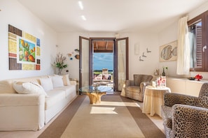 Un salón amplio con un sofá color beige, una mesa de centro de vidrio, sillones estampado de leopardo y vistas al exterior.