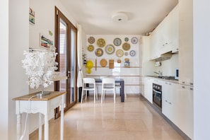 Una cocina con armarios blancos, una mesa de comedor con sillas y una pared decorada con platos.
