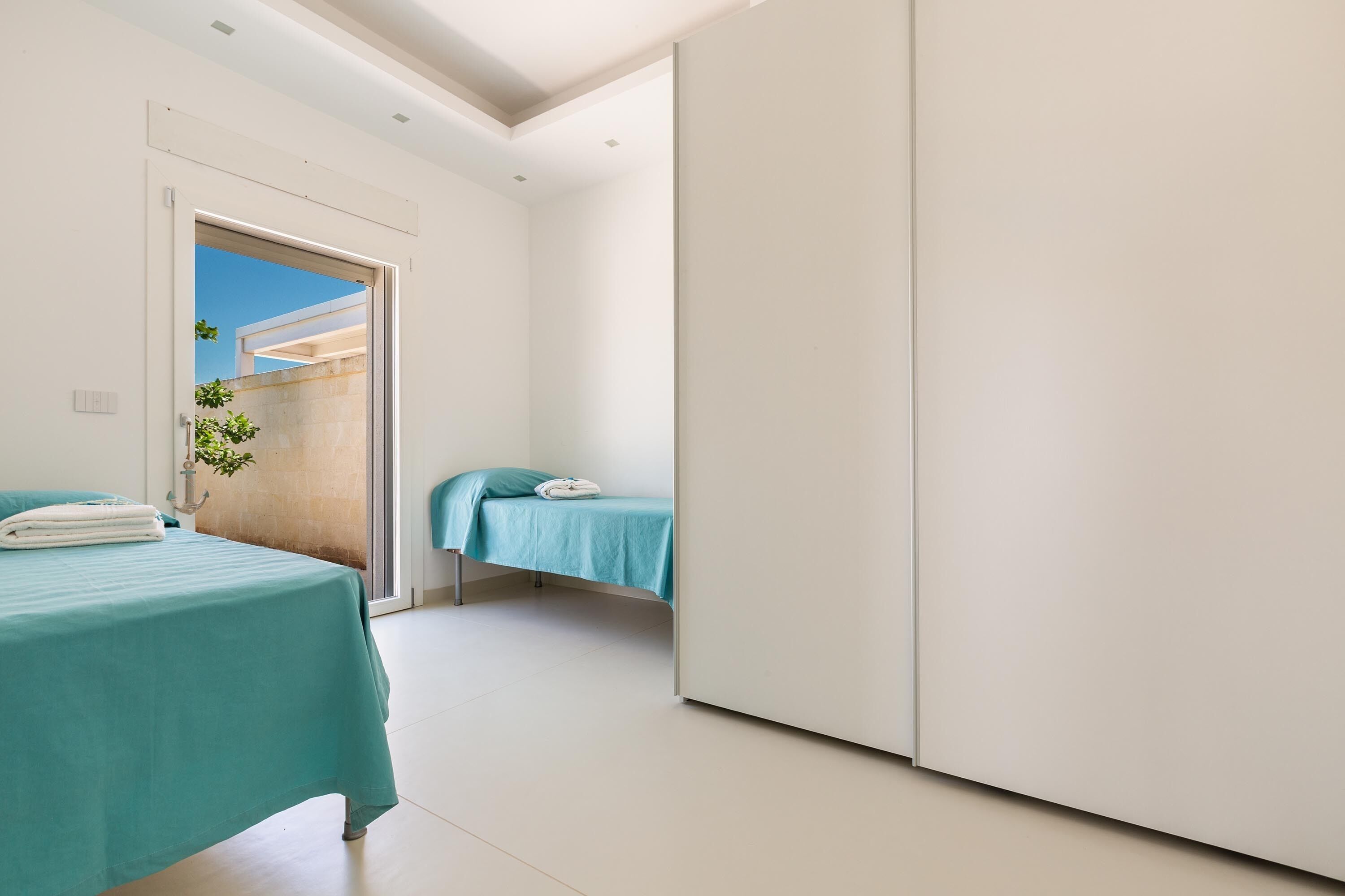A modern bedroom with two beds, a large wardrobe, and a view of the outdoors.
