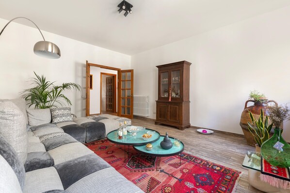Ein Wohnzimmer mit einem Ecksofa, zwei Couchtischen, einem Schrank und einer großen Pflanze.