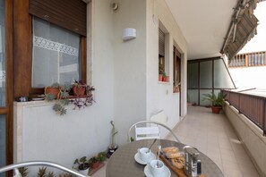 Ein Balkon mit Tisch für zwei Personen, Blumentöpfen und einem Fenster mit Jalousien.