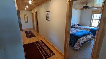 Ein Flur, der in ein Schlafzimmer mit zwei Betten, Holzböden und einem Deckenventilator führt.