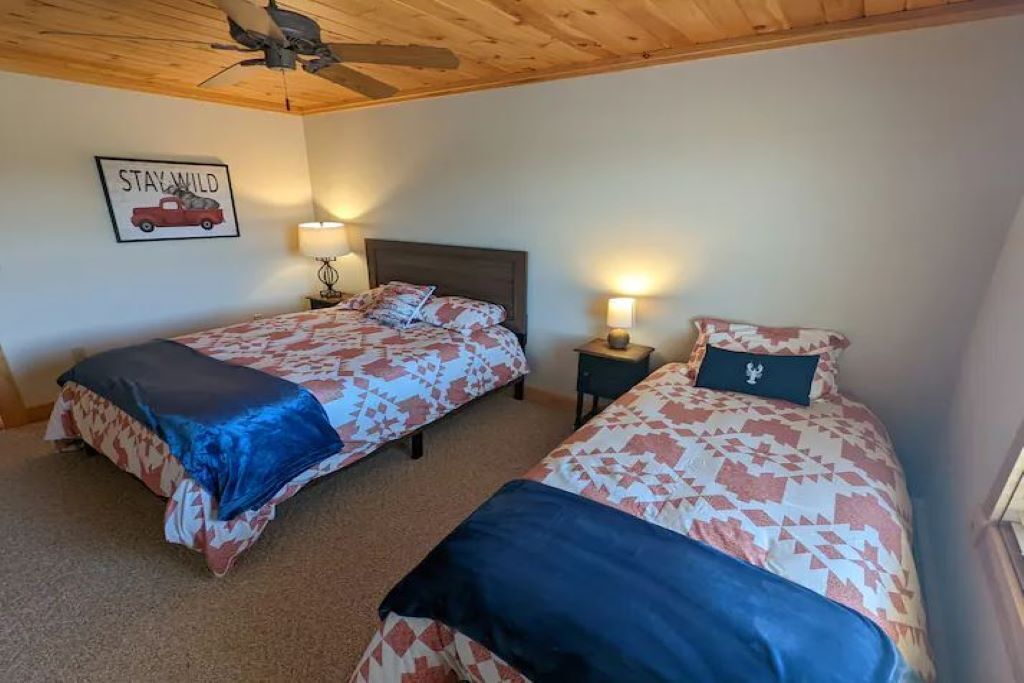 A bedroom with two beds, wooden ceiling, and a 'Stay Wild' sign.