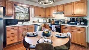 A modern kitchen with wooden cabinets, a central island, and a dining table set for four. - Gatlinburg Mountain View Cabin | Hot Tub & Arcade (Gatlinburg)